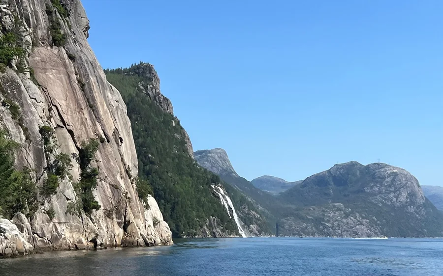 A pale cliff face above the water, a thin waterfall and mountains beyond