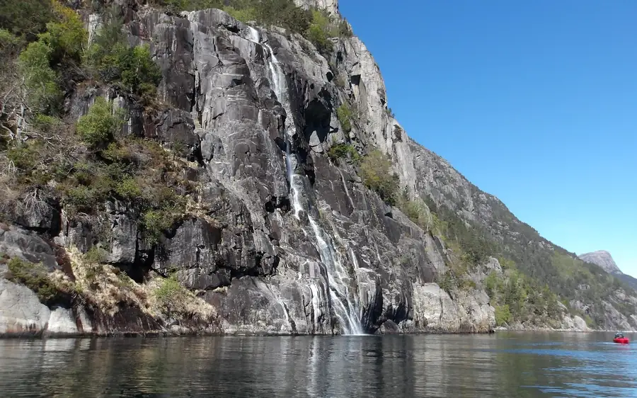 A thin waterfall running down a sheer grey rock wall into still water