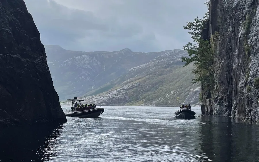 Two inflatable boats with passengers on dark water between steep cliff walls