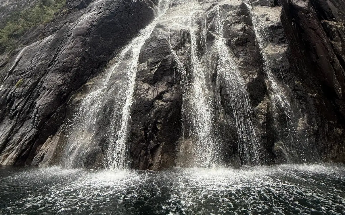 Water fanning down a dark rock face into white spray at the waterline