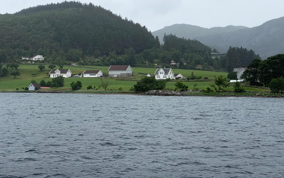 White farmhouses on green fields above grey water, under low cloud