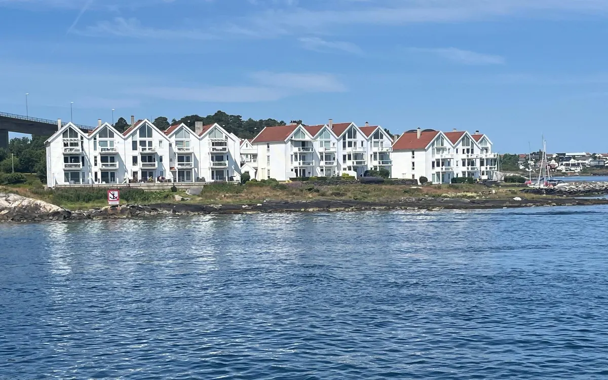 A row of white gabled houses with red roofs on a rocky shore, seen from the water